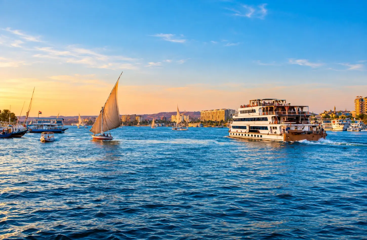 Feluccas and a luxury cruise ship sailing the Nile River at sunset during the best time to visit Egypt