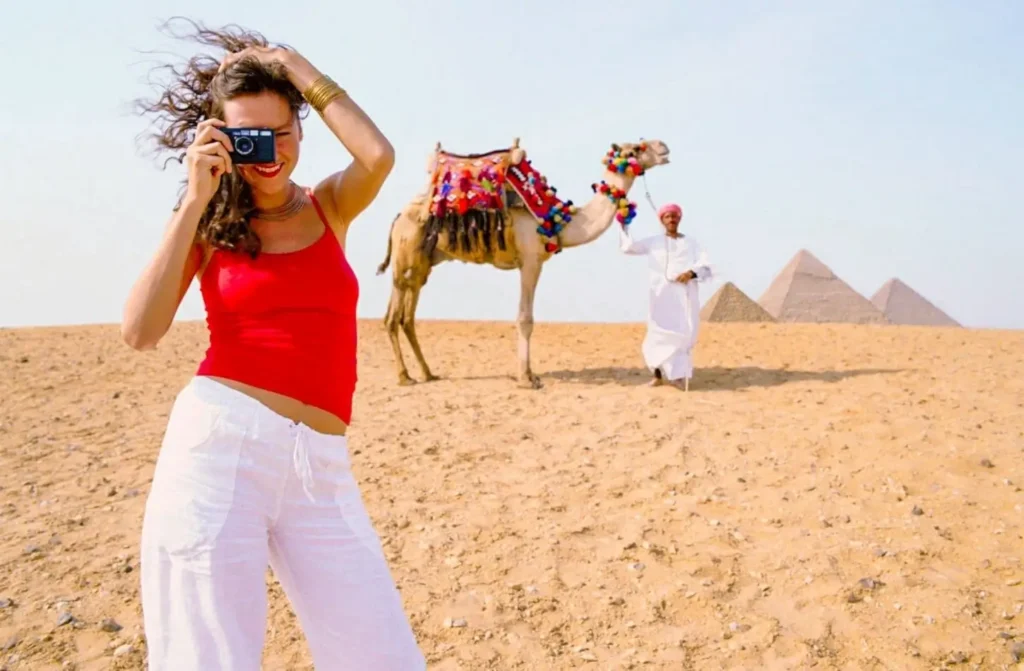 A woman in a white dress riding a decorated camel along a sandy resort beach while visiting Egypt in December.