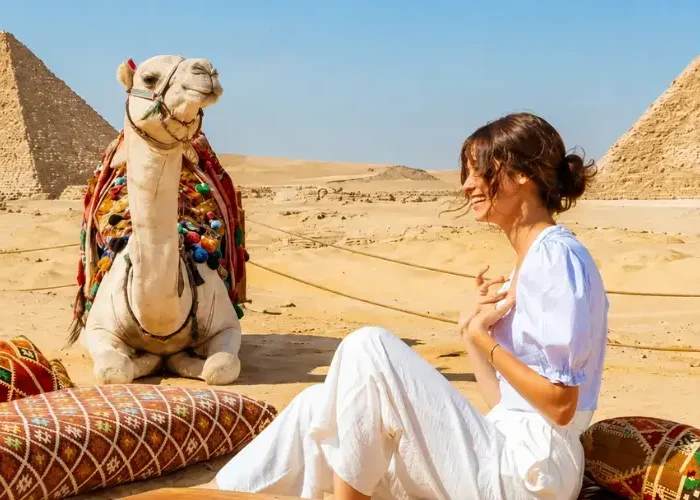 Traveler relaxing on cushions next to a decorated camel in front of the Giza Pyramids during Egypt in October