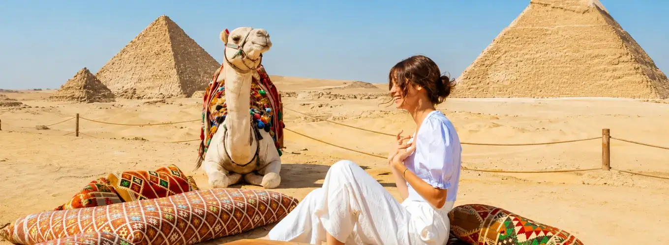 Traveler relaxing on cushions next to a decorated camel in front of the Giza Pyramids during Egypt in October