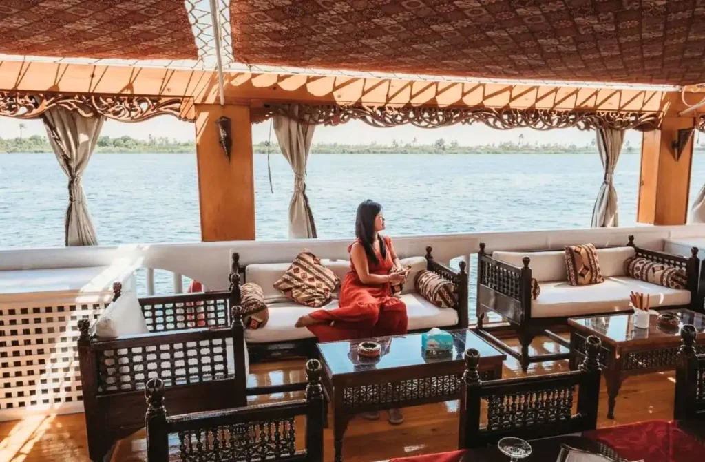 Woman relaxing on the open-air wooden deck of a traditional Dahabiya sailboat, showcasing the intimate atmosphere of a Nile Cruise vs Dahabiya journey.