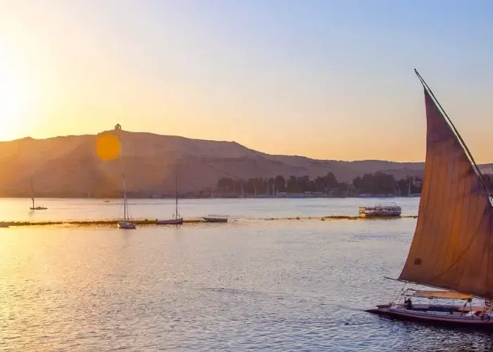 A traditional felucca boat sailing down the Nile River during a golden sunset, perfect for exploring Egypt in November.