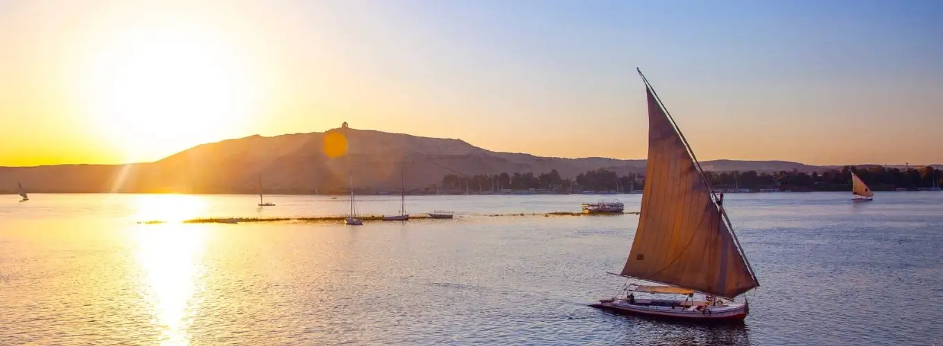 A traditional felucca boat sailing down the Nile River during a golden sunset, perfect for exploring Egypt in November.