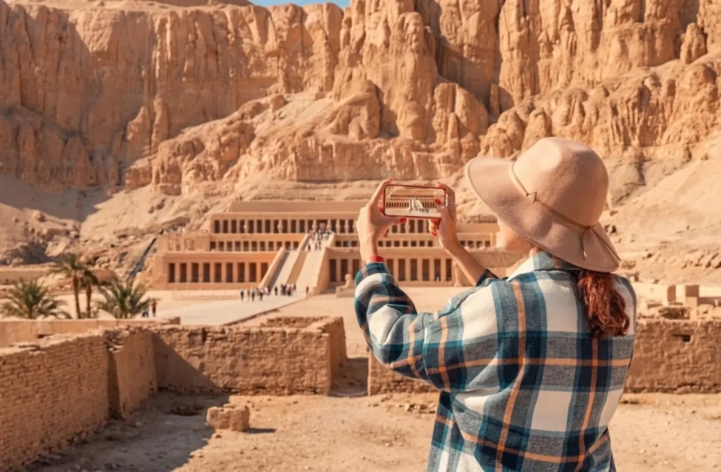 A tourist in a sunhat taking a photo of the Hatshepsut Temple in Luxor while exploring Egypt in January.