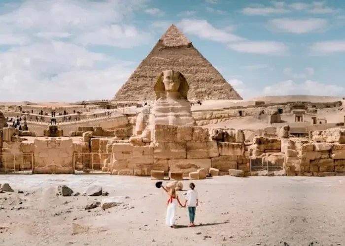 A couple walking towards the Great Sphinx and Pyramids of Giza during a sunny winter day visiting Egypt in January.