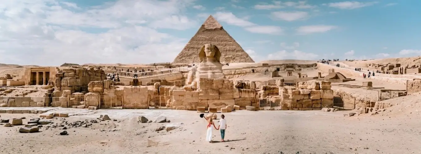 egypt-in-january-pyramids-sphinx A couple walking towards the Great Sphinx and Pyramids of Giza during a sunny winter day visiting Egypt in January.