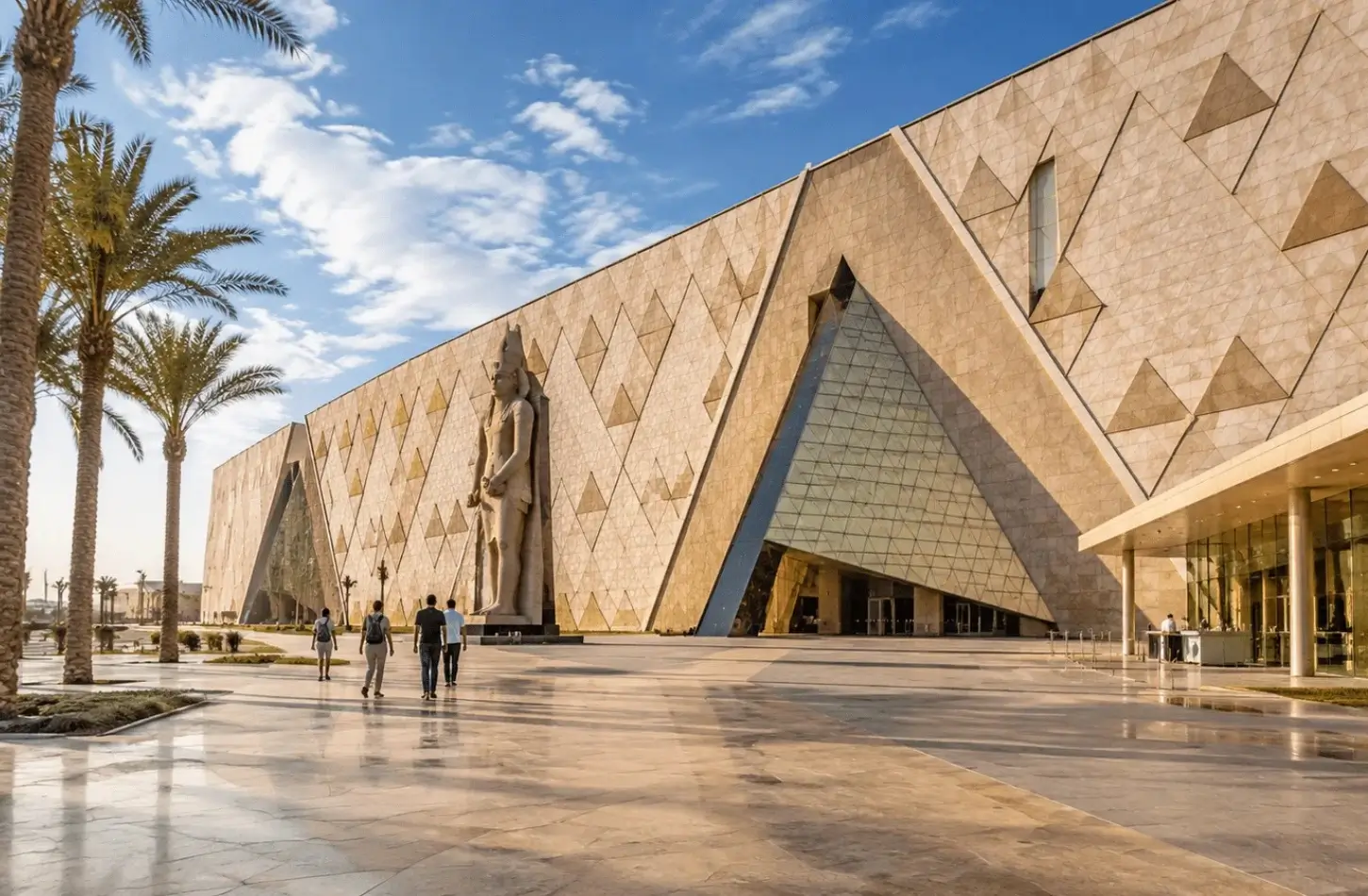 Visitors walking along the outdoor plaza in front of the modern geometric facade of the Grand Egyptian Museum.