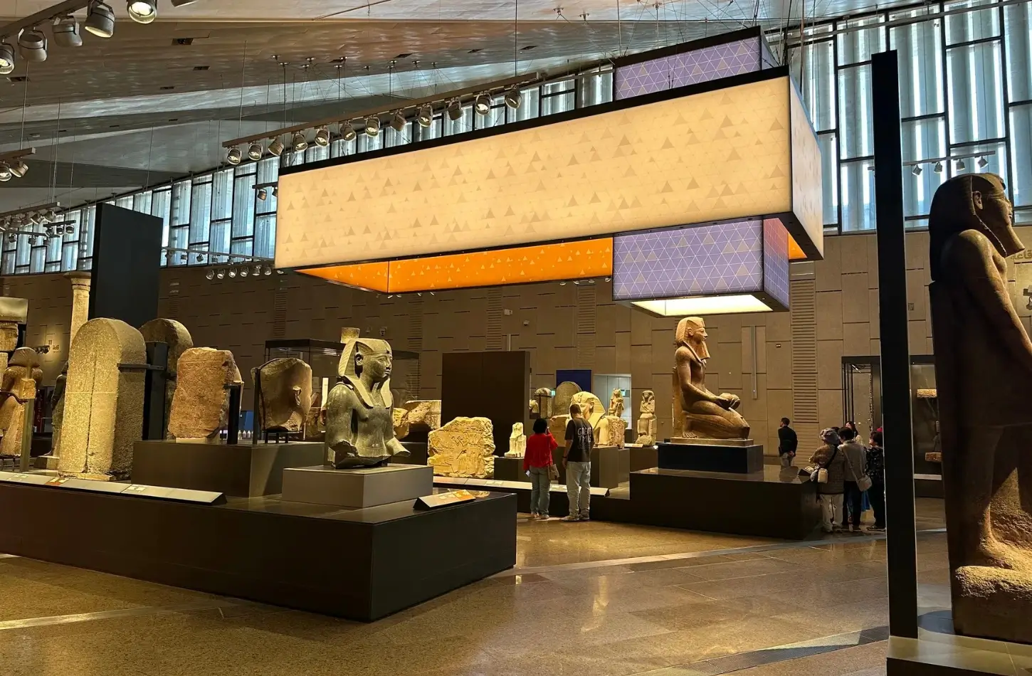 Visitors exploring ancient pharaonic statues inside the main exhibition hall at the Grand Egyptian Museum.
